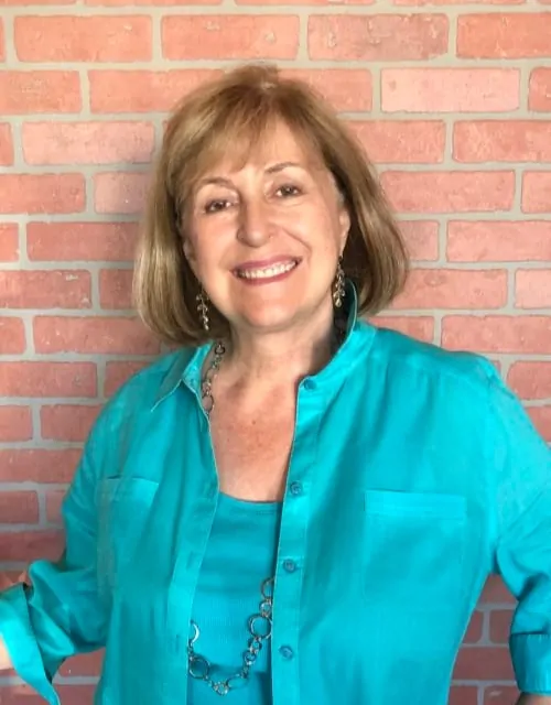 A smiling woman in a turquoise blouse standing in front of a brick wall at a catering company event.