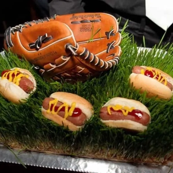 A catering baseball glove holding hot dogs with mustard on a bed of artificial grass in Los Angeles.